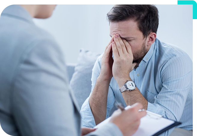 A man with his hands over his face while sitting in front of another person.